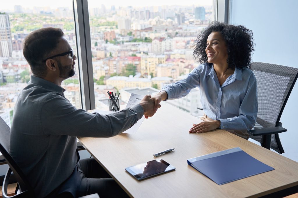 Indian ceo and African American newcomer shaking hands in modern office.
