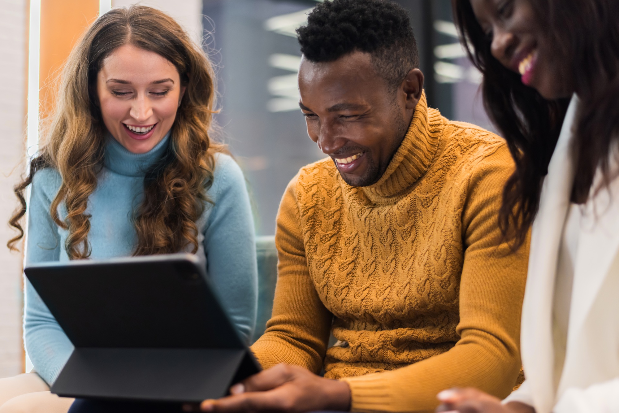 Multiracial group of people in an office discussing business using a tablet while sitting on a sofa